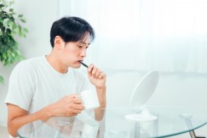 鏡を見ながら歯磨きをする男性の画像