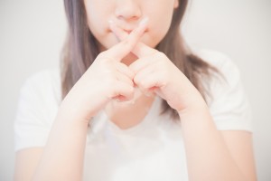 口の前で指をバツにする女性