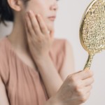 手鏡を見ながら頬を触る女性