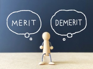 木でできた人形とメリットデメリットの文字