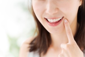 口元を指さしている笑顔の女性