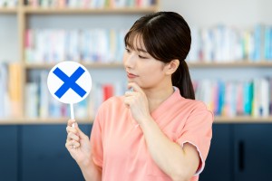 バツマークの札を持つ歯科衛生士