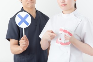 バツの札を持つ歯科医師と歯の模型を持つ歯科衛生士