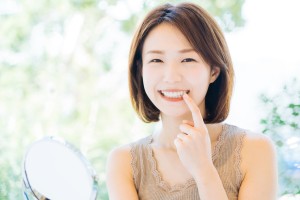 口元を指さしている笑顔の女性